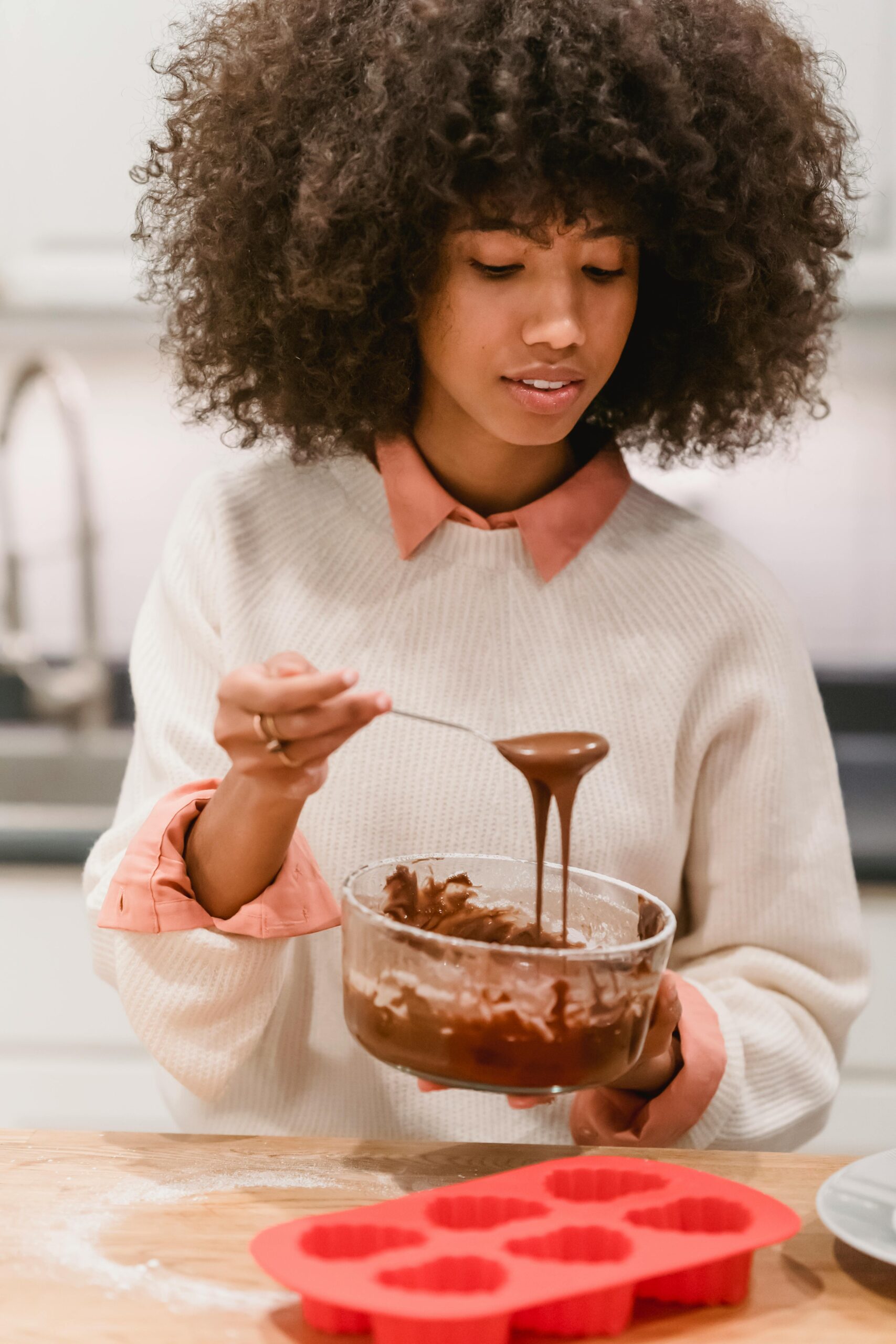 Young woman prepares cake batter using silicone molds in a cozy kitchen setting.